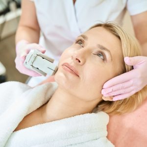 Cropped female cosmetologist doing laser depilation of face of adult woman